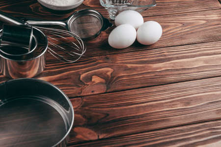 Ingredients in the dishes on a wooden brown table, where as well lie the whisk is full for flour,...