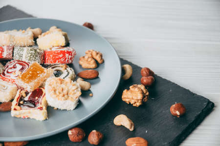 Traditional oriental sweets and nuts: hazelnuts, cashews on a white wooden background. Turkish...