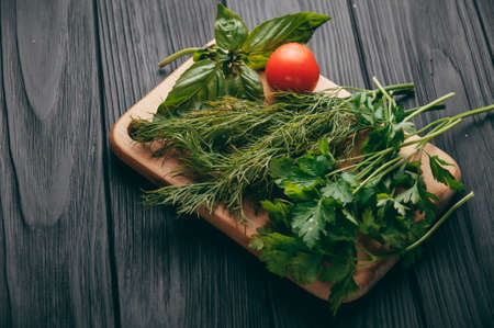 Tomatoes, parsley and dill on a wooden cutting board on a black wooden background.の写真素材