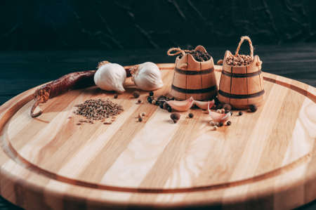 Spices: chili, black pepper, garlic, cumin, coriander, sweet pepper lie on a brown round wooden board on a black table. Place under the textの写真素材
