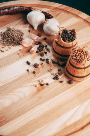 Spices: chili, black pepper, garlic, cumin, coriander, sweet pepper lie on a brown round wooden board on a black table. Place under the textの写真素材