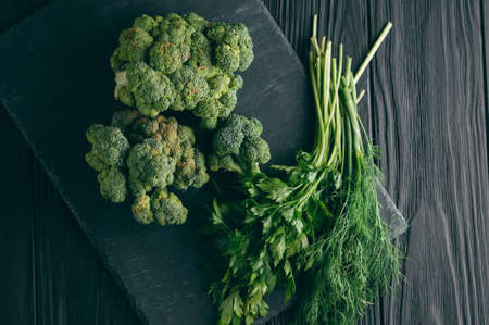 On a dark wooden table, fresh green broccoli, parsley, dill for your health. Flatlay. Recipe. Ingredients. Dietary food. Place under the textの写真素材