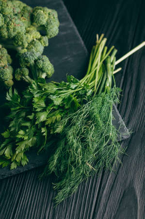 On a dark wooden table, fresh green broccoli, parsley, dill for your health. Flatlay. Recipe. Ingredients. Dietary food. Place under the textの写真素材