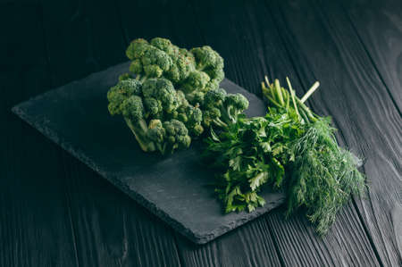 On a dark wooden table, fresh green broccoli, parsley, dill for your health. Flatlay. Recipe. Ingredients. Dietary food. Place under the textの写真素材