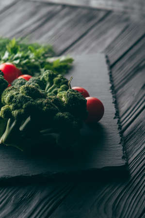 On a dark wooden table, fresh green broccoli, parsley, dill and cherry tomatoes for your health. Recipe. Ingredients. Dietary food. Place under the text. Top viewの写真素材