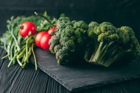 On a dark wooden table, fresh green broccoli, parsley, dill and cherry tomatoes for your health....