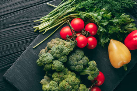 Fresh vegetables: cherry tomatoes, broccoli, pepper, dill, parsley on a dark wooden table. Recipe. Ingredients. Dietary food. Place under the text. View from aboveの写真素材