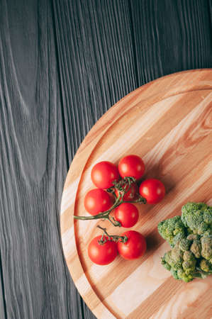 On a dark wooden table, on a round wooden board fresh green broccoli, parsley, dill and cherry tomatoes for your health. Recipe. Ingredients. Dietary food. Place under the text. View from aboveの写真素材