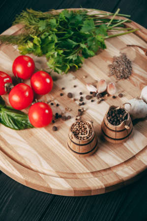 Spices: chili, black pepper, garlic, cumin, coriander, sweet pepper lie on a brown round wooden board on a black table. Place under the textの写真素材