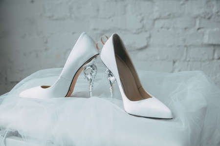 A pair of white wedding shoes with rings on a stoolの写真素材