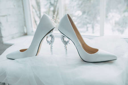 A pair of white wedding shoes with rings on a stoolの写真素材