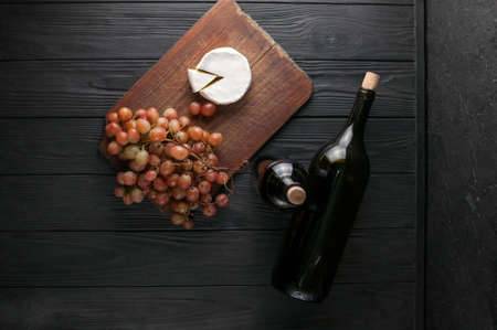 Bottles of wine on a black wooden background with grapes and cheese Camembergの写真素材