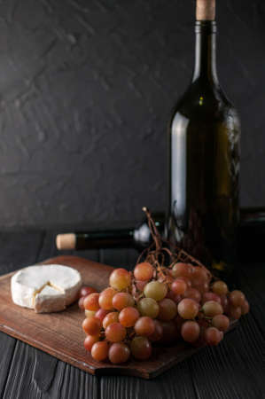 Bottles of wine on a black wooden background with grapes and cheese Camembergの写真素材