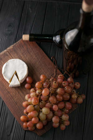Bottles of wine on a black wooden background with grapes and cheese Camembergの写真素材