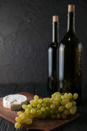 Bottles of wine on a black wooden background with grapes and cheese Camembergの写真素材