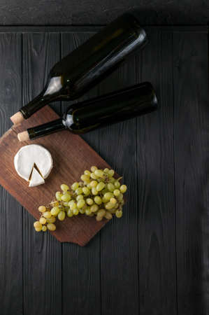 Bottles of wine on a black wooden background with grapes and cheese Camembergの写真素材