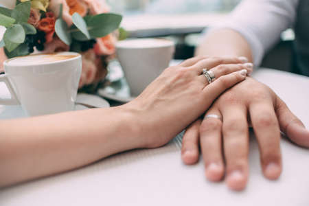 The bride and groom hold hands, holding expensive wedding rings with white gold, on the background...