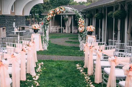 Beautiful wedding set up. Area of the wedding ceremony. Round arch, white chairs decorated with flowers, greenery. Cute, trendy rustic decor. Part of the festive decor, floral arrangement.の写真素材