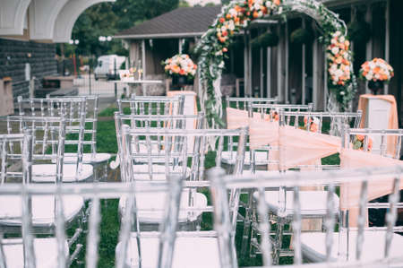 Square wedding ceremony. Transparent chairs are decorated with flowers, greenery. Cute, trendy svdebany decor. Part of the festive decor, flower arrangementの写真素材