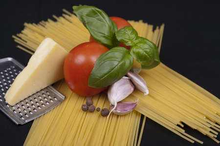 Spaghetti pasta, tomato, basil, garlic, black pepper and cheese isolated on a black background