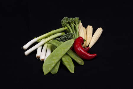 chilli, broccoli, baby leek, baby corn and mange tout on a black background