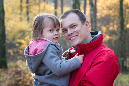 Father holding daughter in autumn forest smiling and looking at the cameraの写真素材