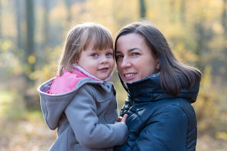 Mother and daughter in autumn forest smiling and looking at the cameraの写真素材