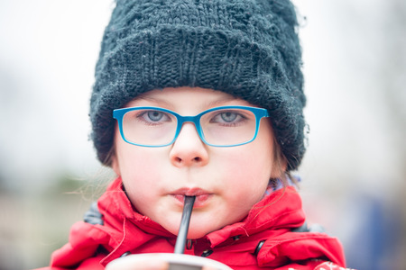 Cute little girl drinking water/juice/ hot chocolate through a straw outdoors - very shallow deep of fieldの写真素材