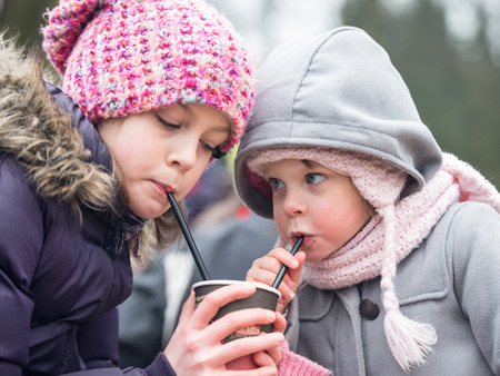 cute little sisters drinking water/juice/ hot chocolate through a straw outdoors - very shallow deep of fieldの写真素材
