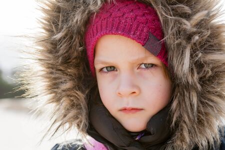 portrait of serious girl wearing fur hood looking at camera outdoorの写真素材