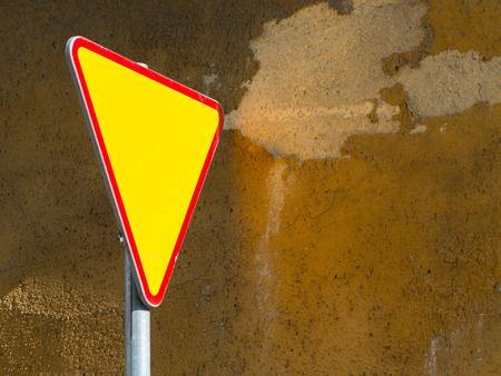 Give way sign - yield sign - against rough  mustard wall backgroundの写真素材