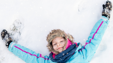Happy child girl laying down on a frozen clear snow -  playing games during a sunny winter vacation - winter funの写真素材