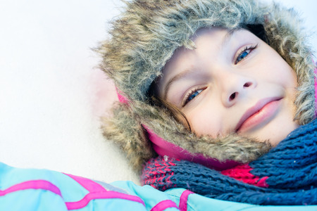 Happy child girl laying down on a frozen clear snow -  playing games during a sunny winter vacation - winter funの写真素材