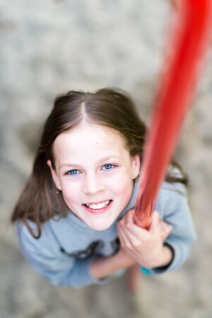Young smiling amused pretty hipster girl is wearing warm gray blouse on the playground, summer time...