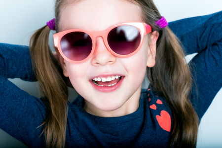 Cheerful smiling cute child with teeth dropped out - preschooler girl in sunglasses with open mouth without milk toothの写真素材