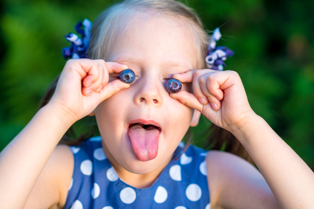Smiling girl holding blueberries in front of her face - showing her tongue - covering eyes with berriesの写真素材
