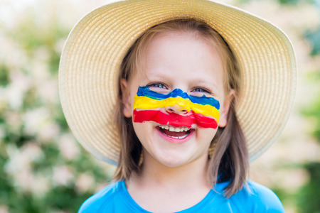 Laughing little girl in straw hat with painted face having fun. Outdoor portraitの写真素材
