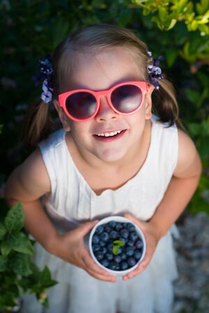 Little girl in sunglasses holding a bowl of blueberries - shallow depth of field - top viewの写真素材