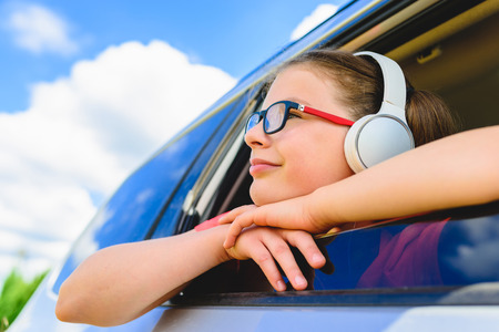 Cute girl listening to music with headphones - looking through open window of the carの写真素材