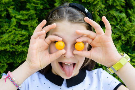 Portrait of young, smiling, happy girl holding, showing small tomatoes over her eyes, laughing....