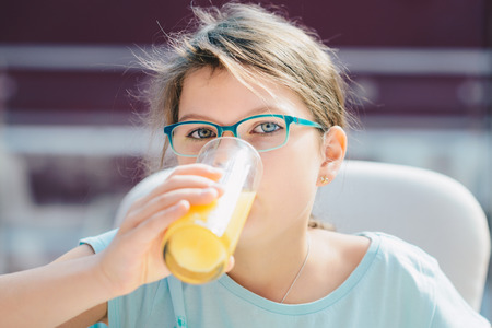 Portrait of a pretty child girl holding glass with tasty orange juice. Healthy Lifestyle, Vegetarian...