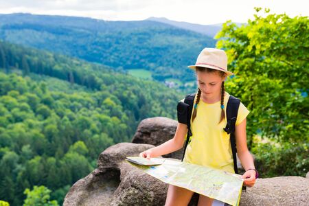 Young hipster tourist girl holding and looking map on trip; lifestyle concept adventure, traveler with backpack on background mountain landscape horizon, young girl hiker pointing hands on trekking planの写真素材