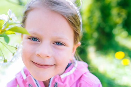 little laughing girl in pink jacket squinting eyes on a spring background with blooming flowers of cherriesの写真素材