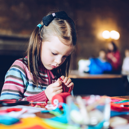 tailor art workshops for children - a girl sewing felt decorations - colorful fabrics lying on a table - a little girl slipping a needleの写真素材