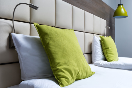 Green pillow, reading lamps and leather bed headboard in modern bedroomの写真素材