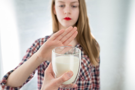 Lactose intolerance. Dairy Intolerant young girl refuses to drink milk - shallow depth of field. Selective focus on glass of milkの写真素材