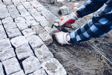 industrial worker installing pavement rocks, cobblestone blocks on road pavementの写真素材