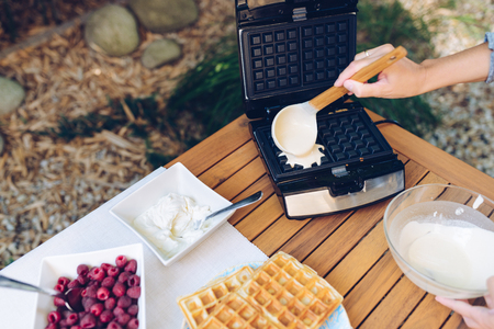 Preparation of homemade waffles. Pouring dough into waffle irons with a ladle outdoors in the gardenの写真素材
