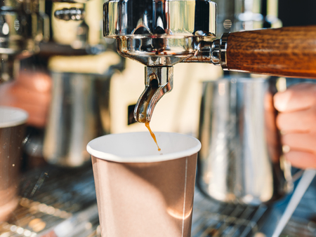 Espresso machine brewing a coffee - golden espresso flowing into the brown paper cup 