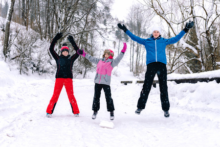 Three friends joyfully jump over snowdrifts in the winter in the mountain forest